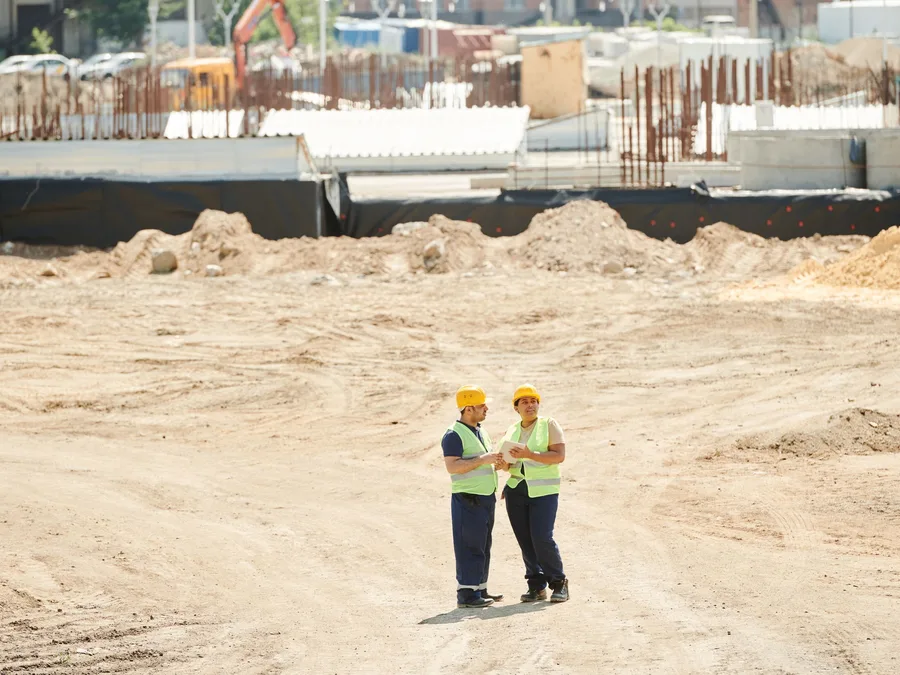 Dos ingenieros revisando planos en un terreno en obra (imagen ilustrativa)